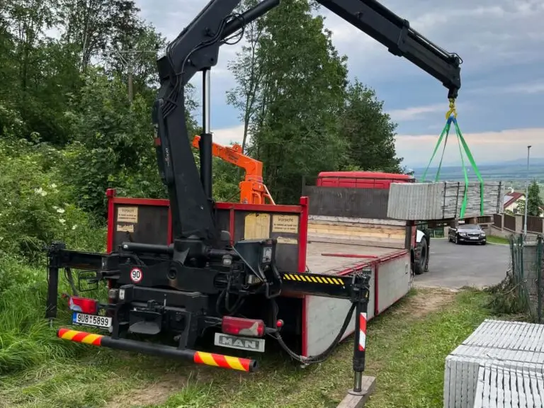 Hydralická ruka vykládá z nákladního vozu betonové stěny.